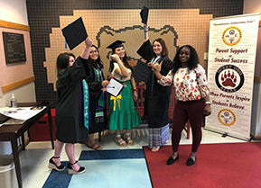 recently graduated student teachers posing in their caps and gowns in the foyer